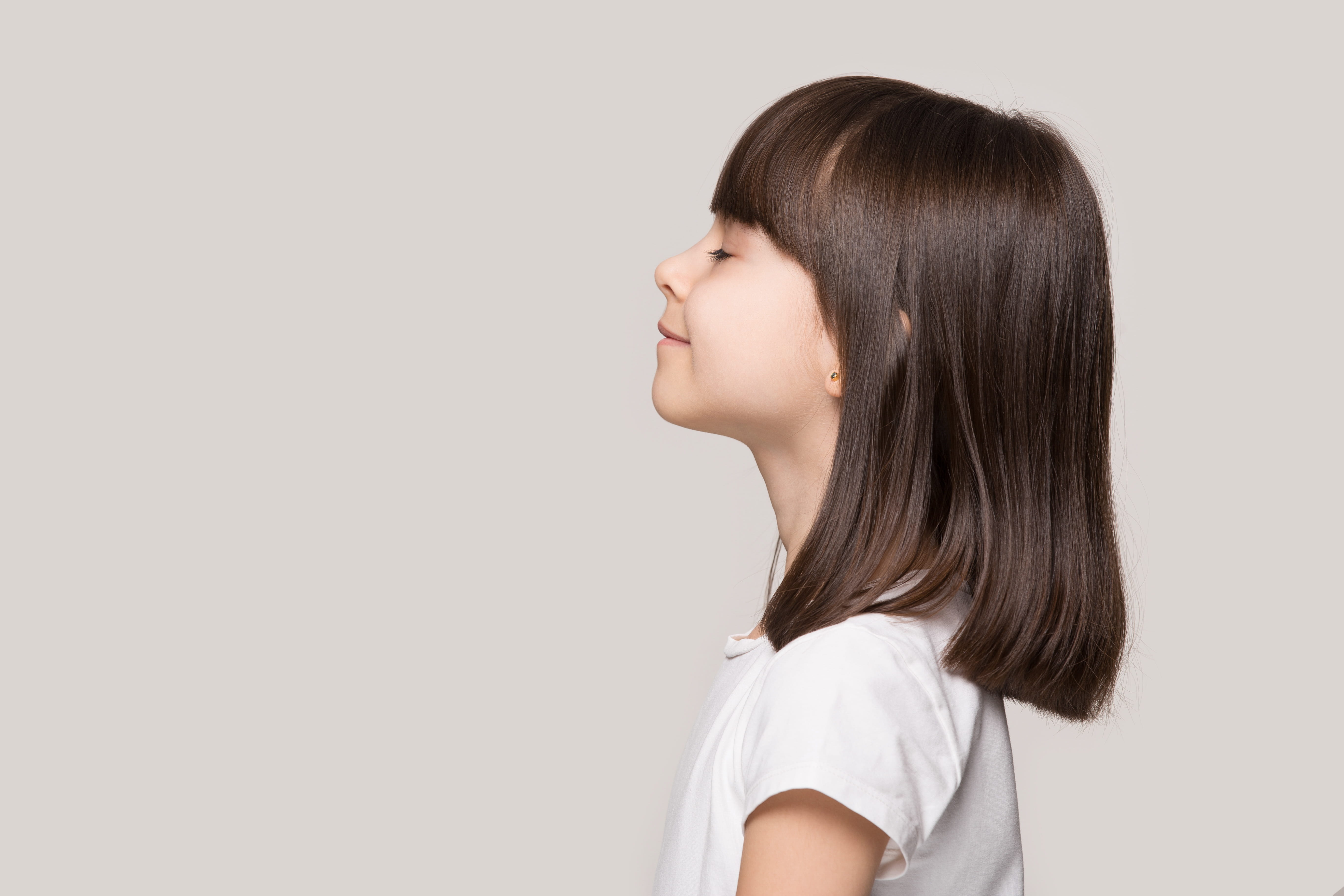 Profile side view face brown-haired little girl standing isolated on beige studio background, smiling with good, healthy energy feeling 