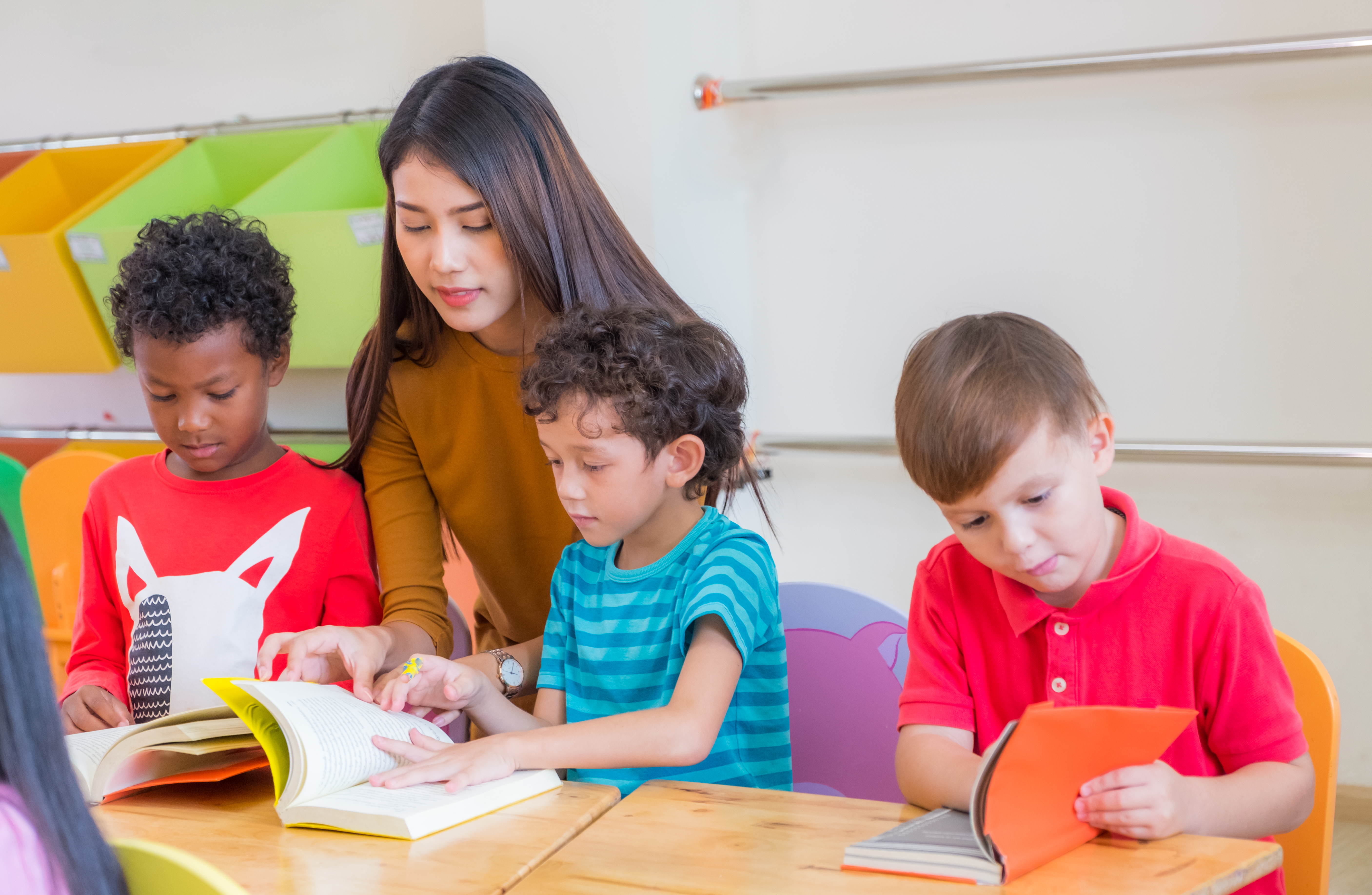 Asian female teacher teaching diversity kids reading book in classroom, Kindergarten pre school concept