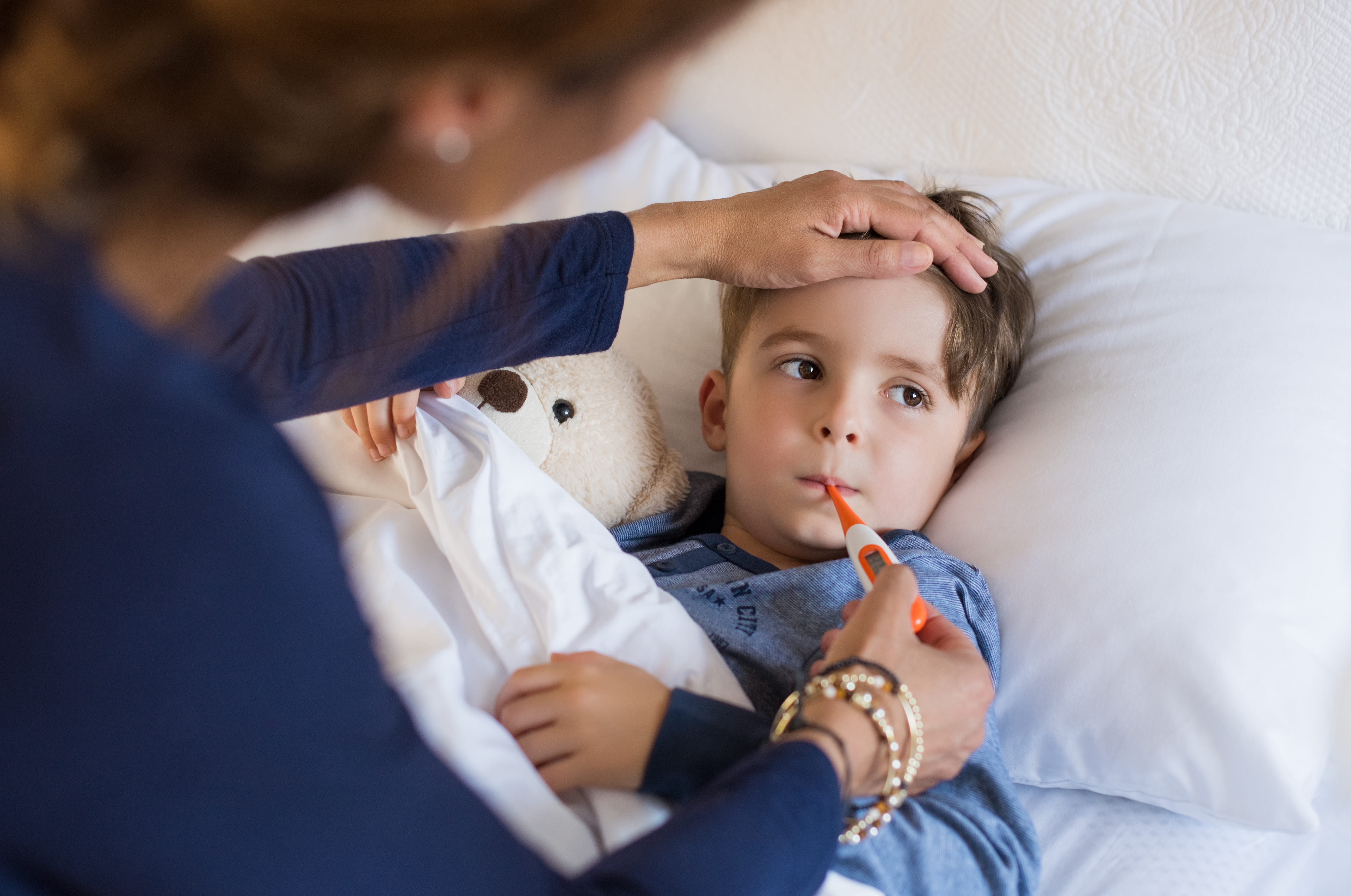 Mother checking temperature of her sick son who has thermometer in his mouth.
