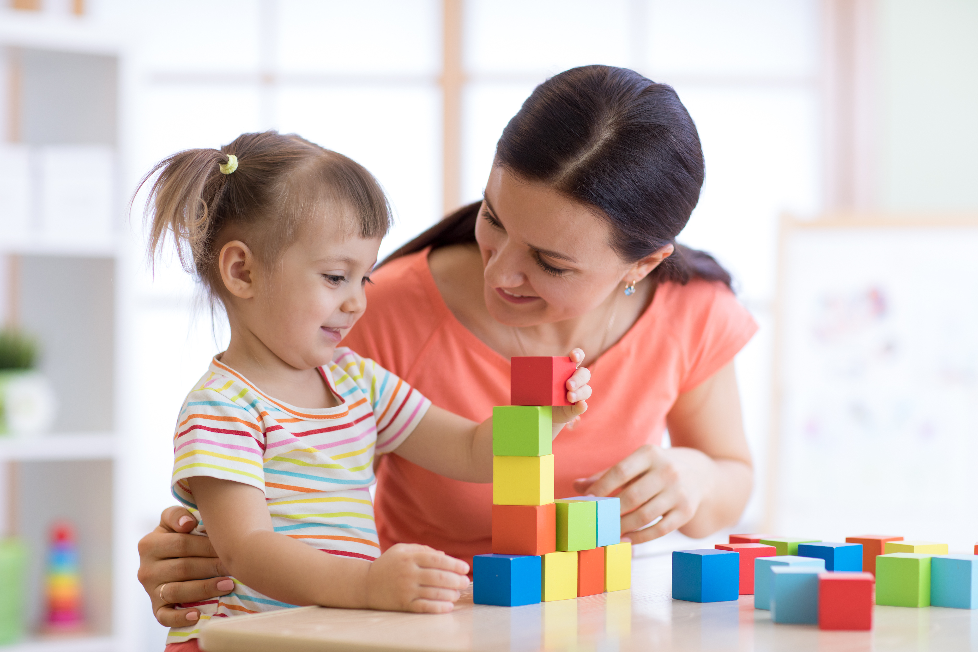 Lady and kid girl playing educational toys at kindergarten or nursery room