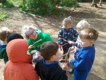 Lady with group of young children in a park / woodland area, holding sticks