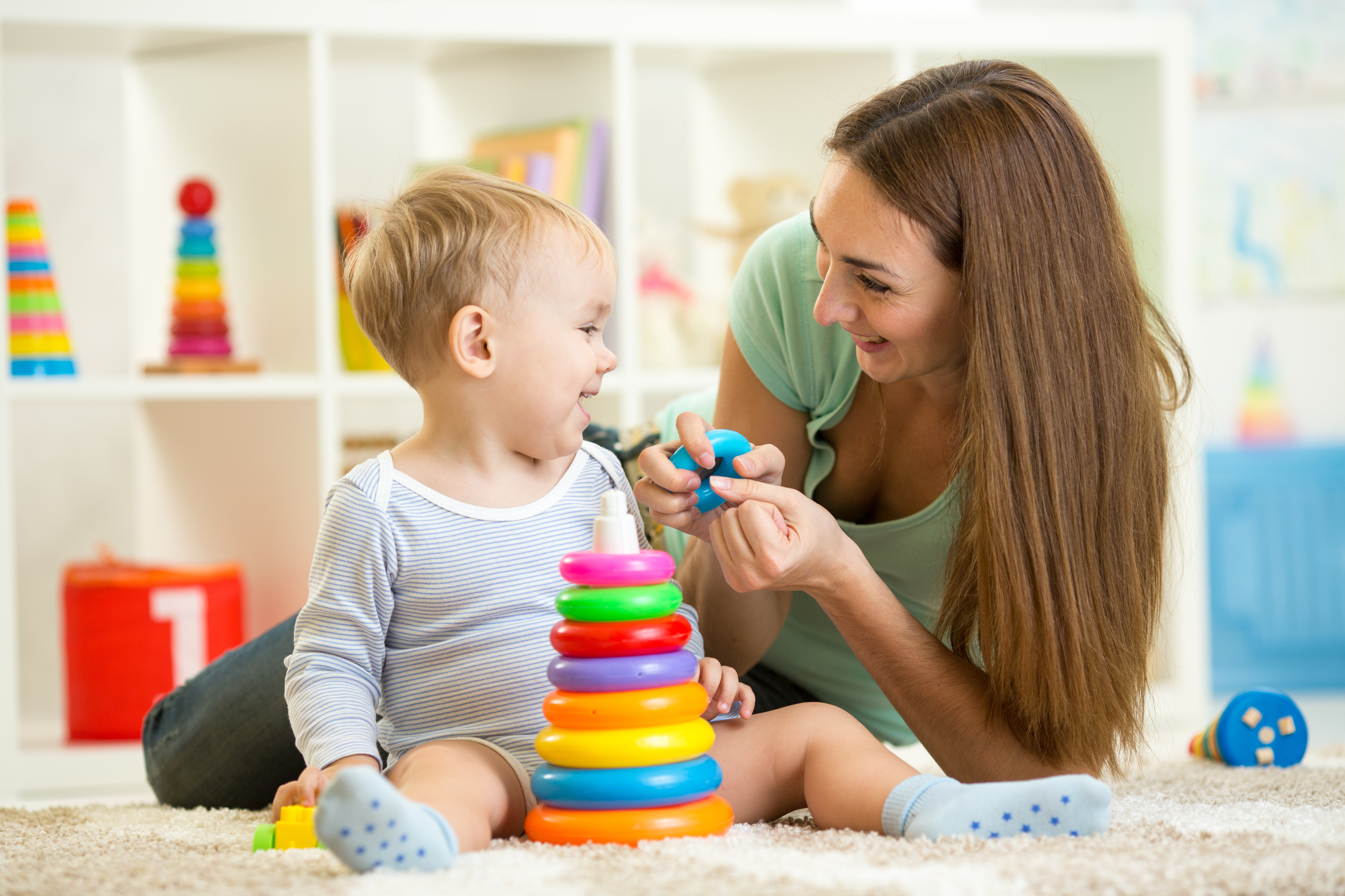 Childminder and toddler smiling, playing with coloured toy rings 