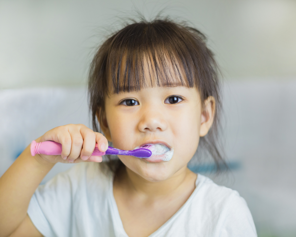 Young girl child brushing her teeth with pink and purple toothbrush
