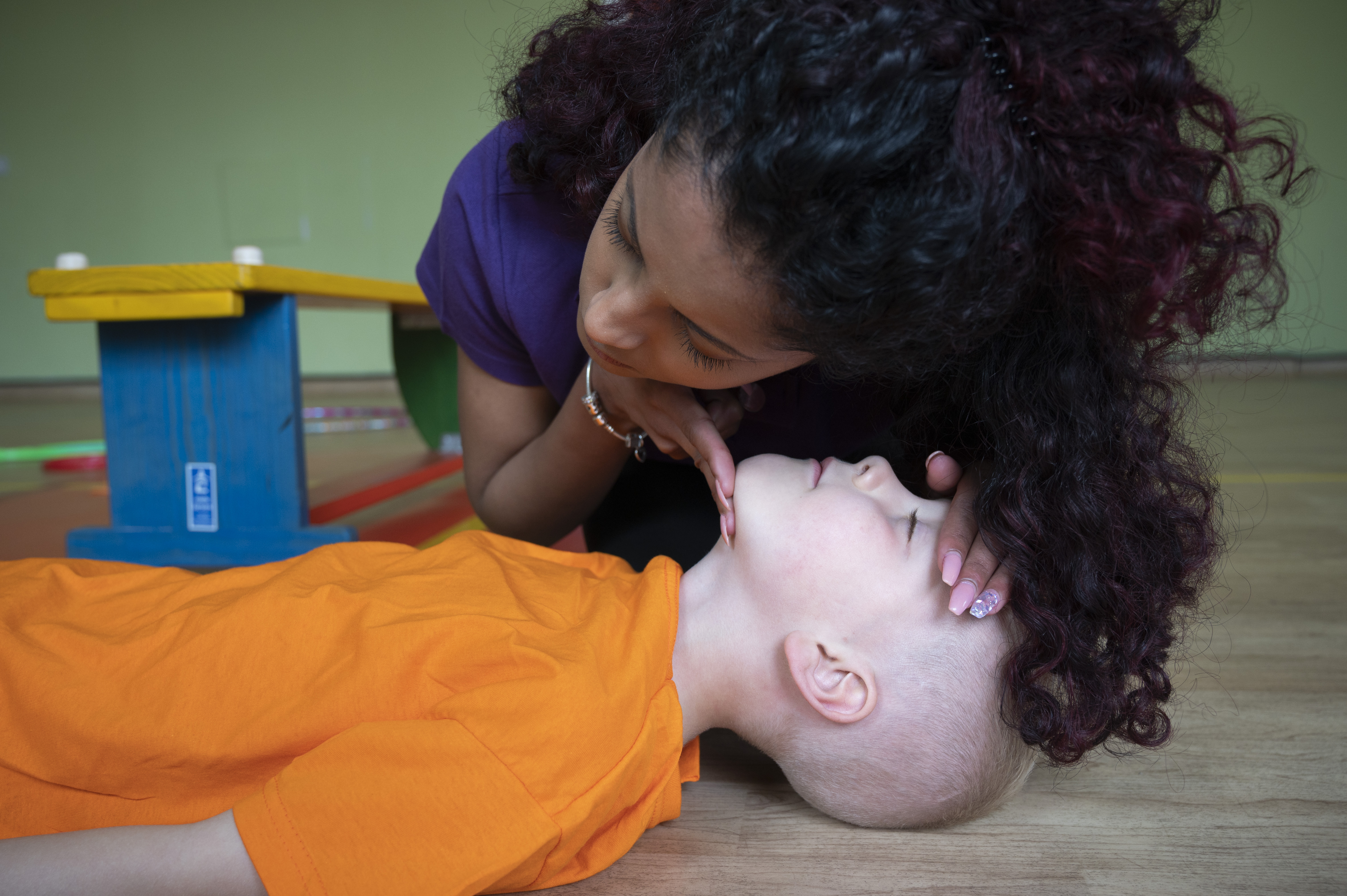 Woman checking if child lying on floor is breathing by looking, feeling and listening for breaths