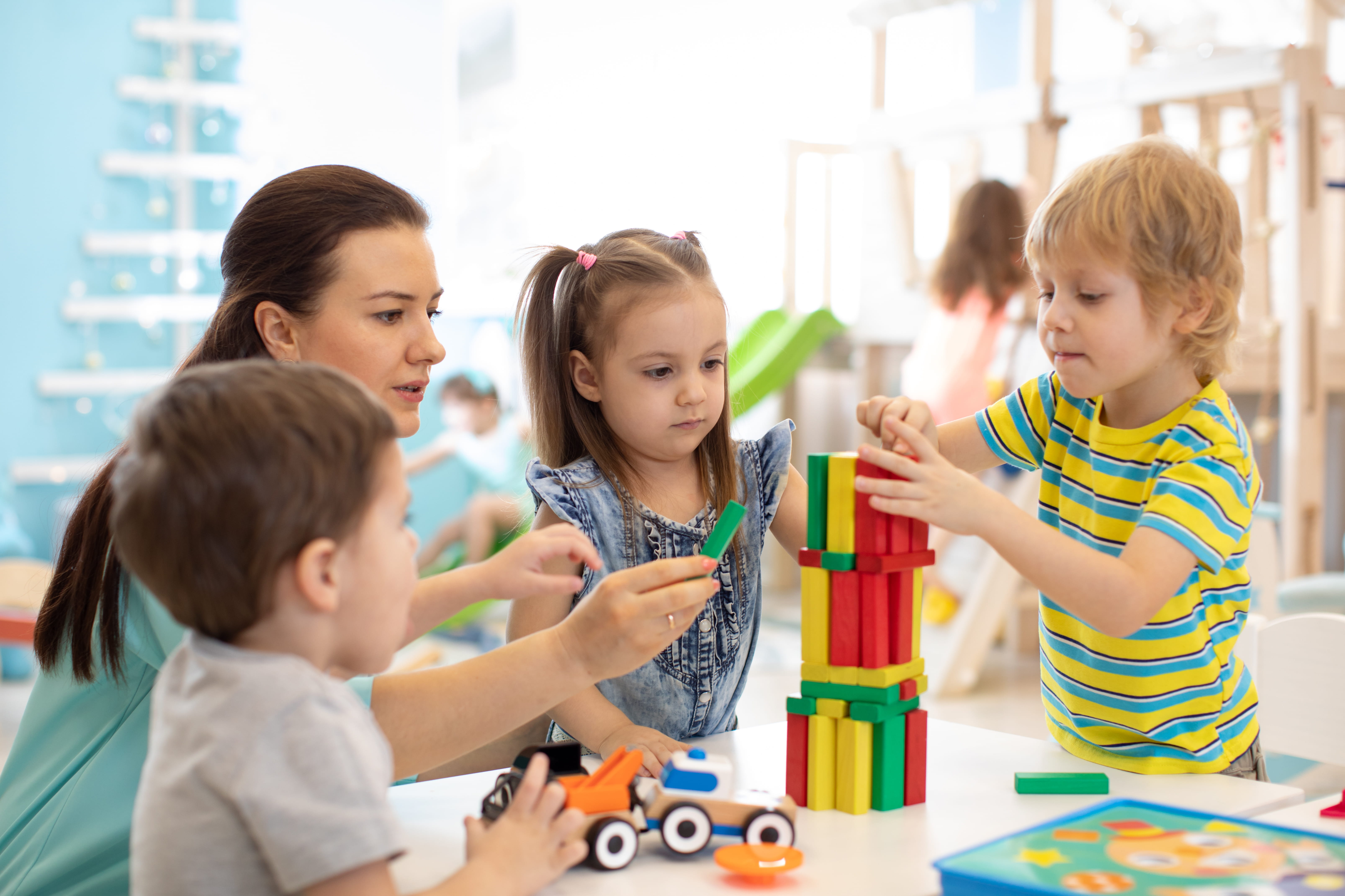 Young kindergarten children playing with educational toys at preschool with teacher helping them