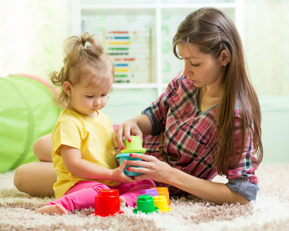 Kid toddler sitting on the floor with babysitter playing with colourful blocks together 