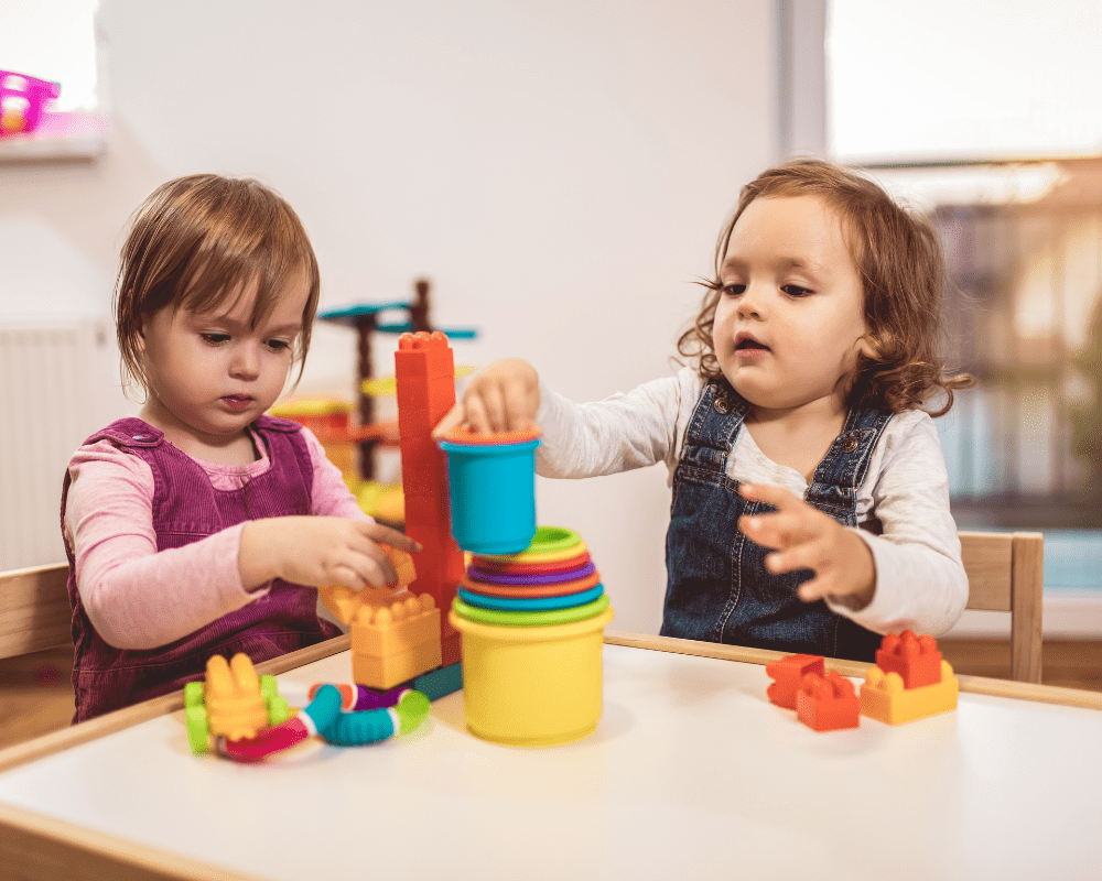 Two toddler girls playing with toys at home, kindergarten or nursery