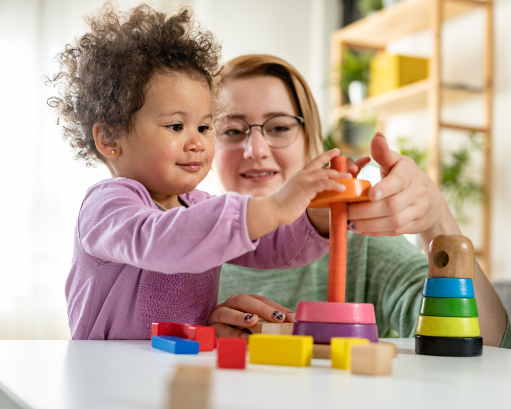 Mother or childcarer with toddler playing with a colourful and educational didactic toy 