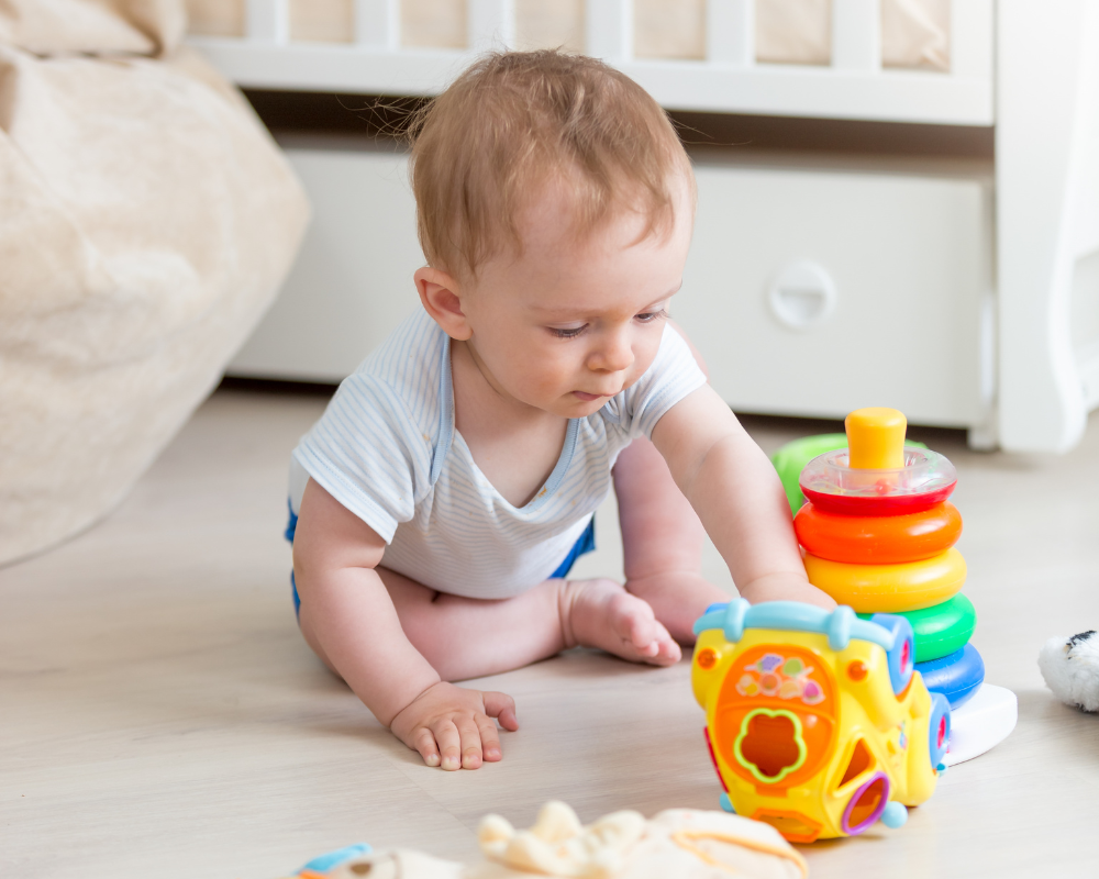9 months old baby playing with colourful toys on the floor in bedroom 